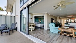 A spacious living area with a large sliding glass door leading to a bedroom, a ceiling fan, and a dining area with chairs and a table.