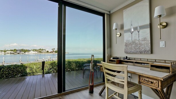 A balcony with a view of the sea, a wooden desk, a chair, and a wall-mounted lamp.