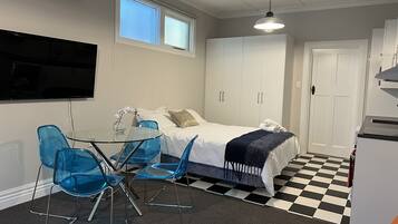 A compact room with a bed, a small table with chairs, a television mounted on the wall, and a refrigerator.