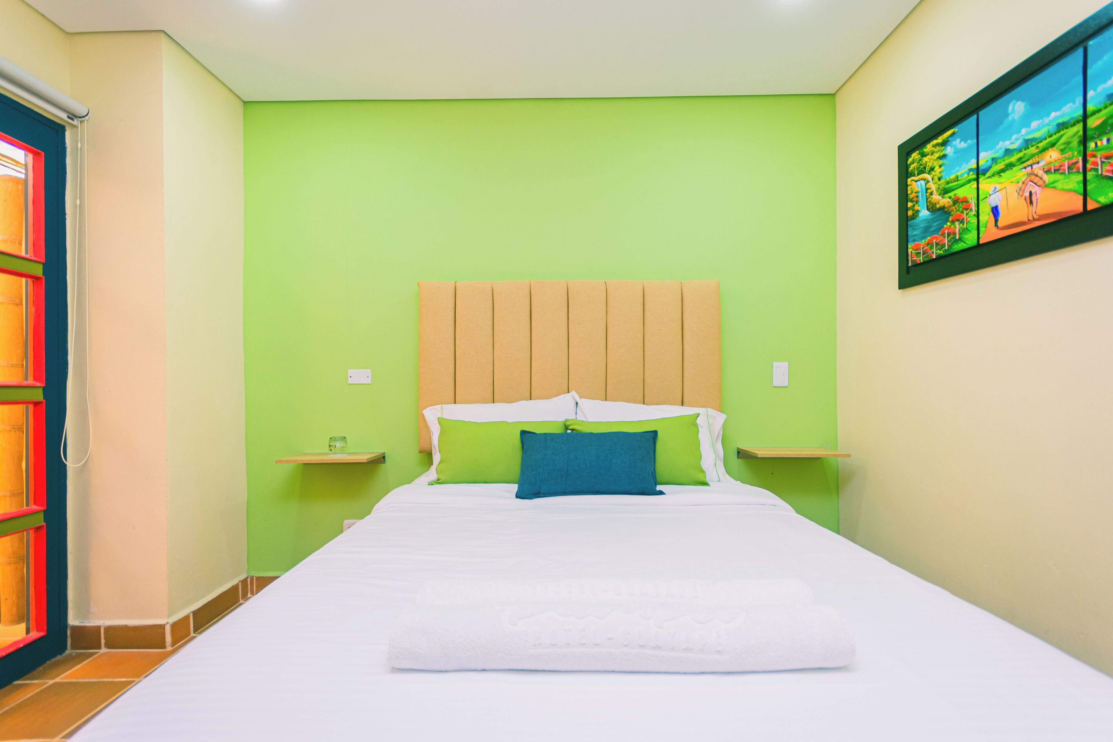 A hotel room with a large bed, green walls, a wooden headboard, and a painting on the wall.
