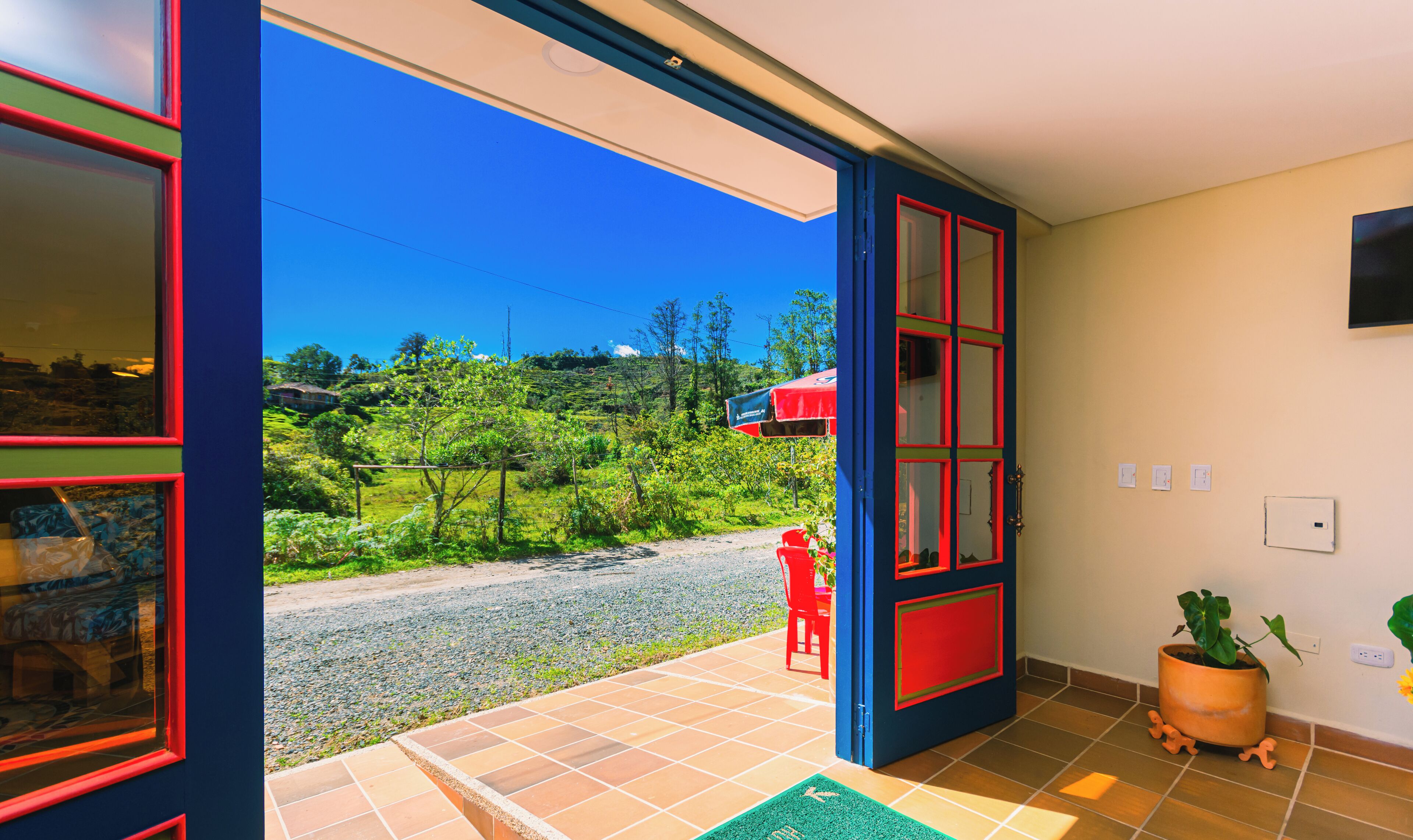 A room with a large sliding glass door leading to a balcony with a view of a green landscape and a red umbrella.