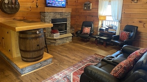 Ein gemütliches Blockhaus-Interieur mit Kamin aus Stein, Ledersitzmöbeln, einem Fernseher und Holzwänden.