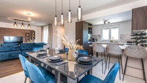 A modern kitchen with a central island, bar stools, and a dining area with a marble table and blue chairs. - Pet friendly home in Tinj (Tinj)