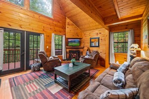 Cozy cabin interior with a high ceiling, comfortable seating area, and a fireplace.