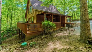 Une cabane en rondins dotée d’une terrasse, entourée de forêt.