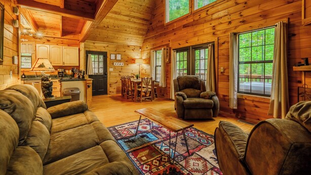 L’intérieur d’une cabane en rondins comprend un salon, un coin repas, une cuisine et de grandes fenêtres.