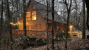 Une cabane en rondins dotée d’une terrasse, entourée d’arbres et recouverte de feuilles mortes.