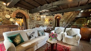 A cozy living room with a stone wall, wooden beams, a white sofa with patterned cushions, a small table with a vase of flowers, and a red patterned rug. - Beautiful private villa with private pool, hot tub, A/C, WIFI, TV, panoramic view, close to Cortona (Sant'angiolo)