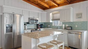 A kitchen with white cabinets, stainless steel appliances, a wooden ceiling, and a green tiled backsplash. - Oak Island Beachfront Bungalow - Direct Ocean Views + Sleeps 8 (Oak Island)