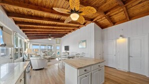 A spacious kitchen with wooden beams, a large island, and a dining area with a view. - Oak Island Beachfront Bungalow - Direct Ocean Views + Sleeps 8 (Oak Island)