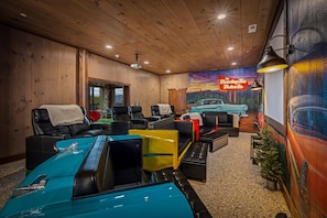 Een kamer met houten wanden en plafond, een muurschildering van een auto aan de muur, en een model van een oldtimer op de voorgrond.