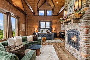 A cozy log cabin interior with a fireplace, a bed, a sofa, and a dining table. - Welcome to Dancing Fox! Luxury 7BR, Indoor Pool, Fire Pit, Wow Views!!! (Sevierville)