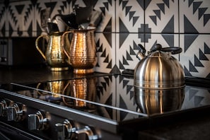 Een keuken met een spiegelende kookplaat, een waterkoker en een koffiepot op het aanrecht.