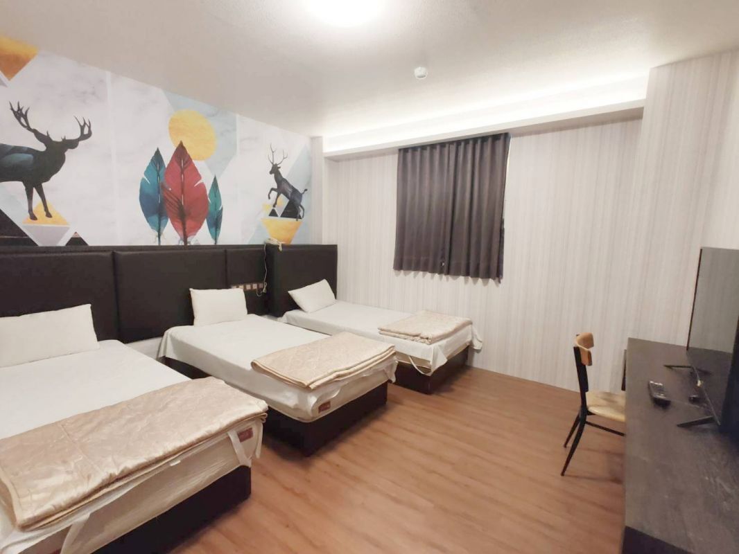 Habitación de hotel con tres camas, un escritorio, una silla y un cuadro abstracto grande en la pared.