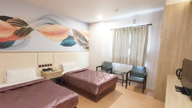 A hotel room with two beds, a small table, a chair, a TV, and a decorative wall mural.
