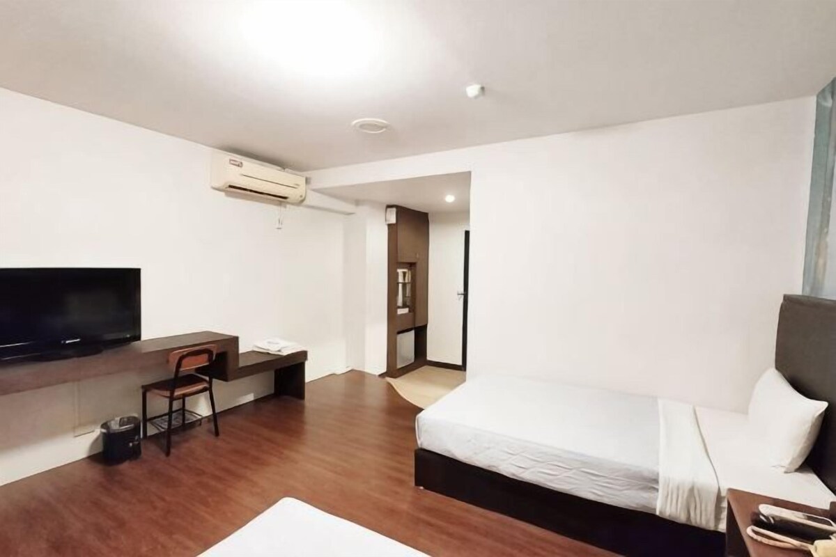 A hotel room with a bed, a desk with a chair, a TV, and an air conditioning unit.