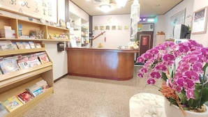 A reception area with a wooden desk, a chandelier, and shelves with books and magazines.