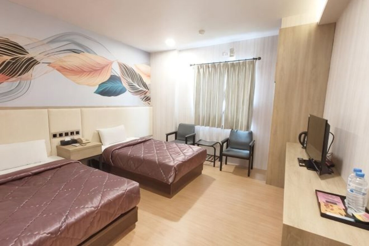 A hotel room with two beds, a desk with a computer, a chair, and a window with curtains.