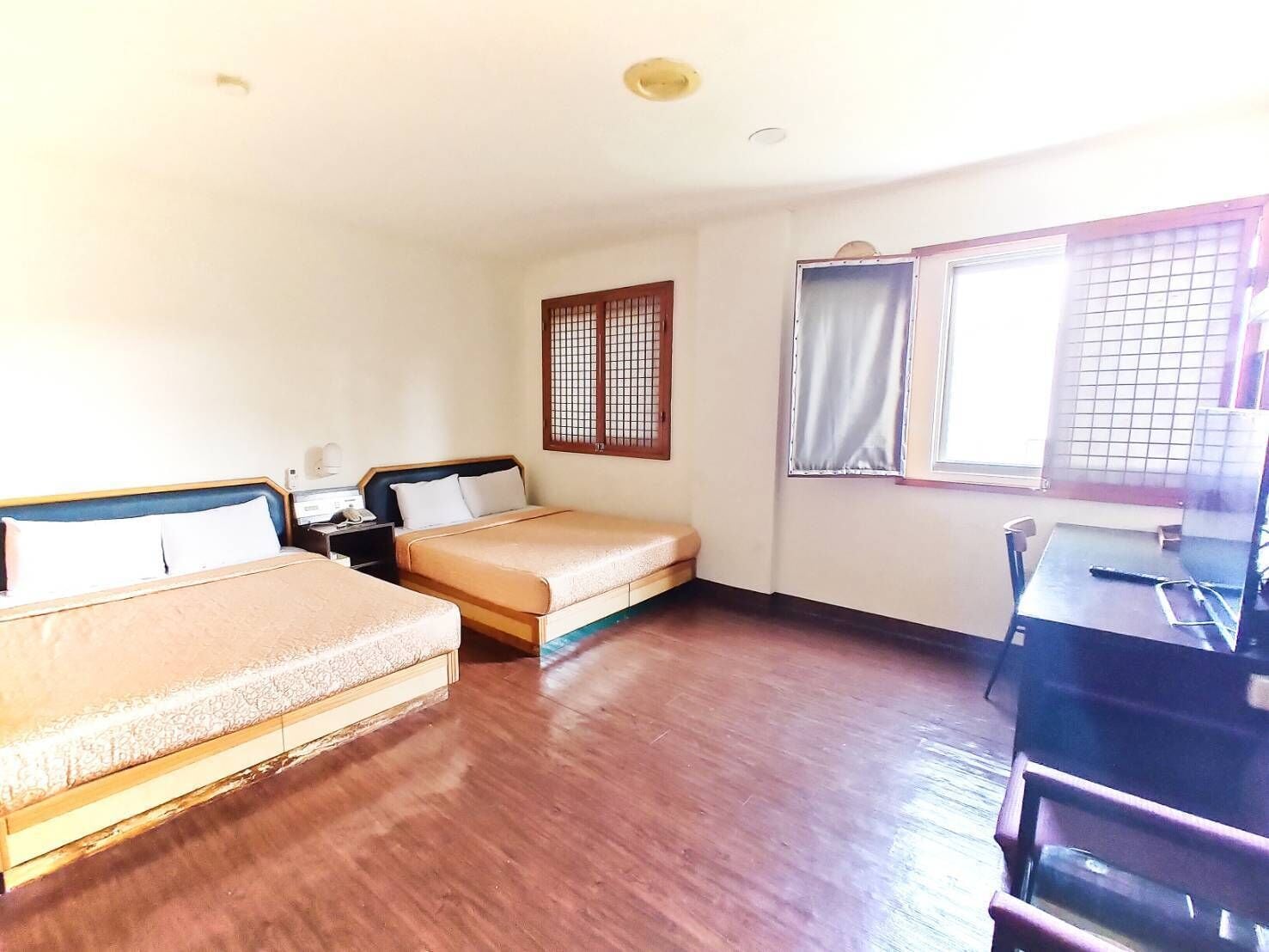 Una habitación de hotel con dos camas, un escritorio, una silla, una ventana con cortinas y suelo de madera.