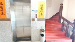An elevator, a staircase, and a trash bin with a plant.