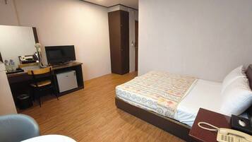 A hotel room with a bed, a desk with a computer, a telephone, and a small refrigerator.