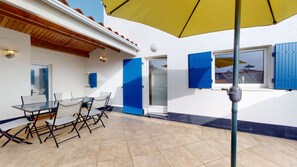 Ein Patio mit einem Glastisch und Stühlen, einem gelben Sonnenschirm und blauen Fensterläden.