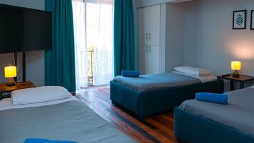 Habitación de hotel con dos camas, televisor y balcón con cortinas.