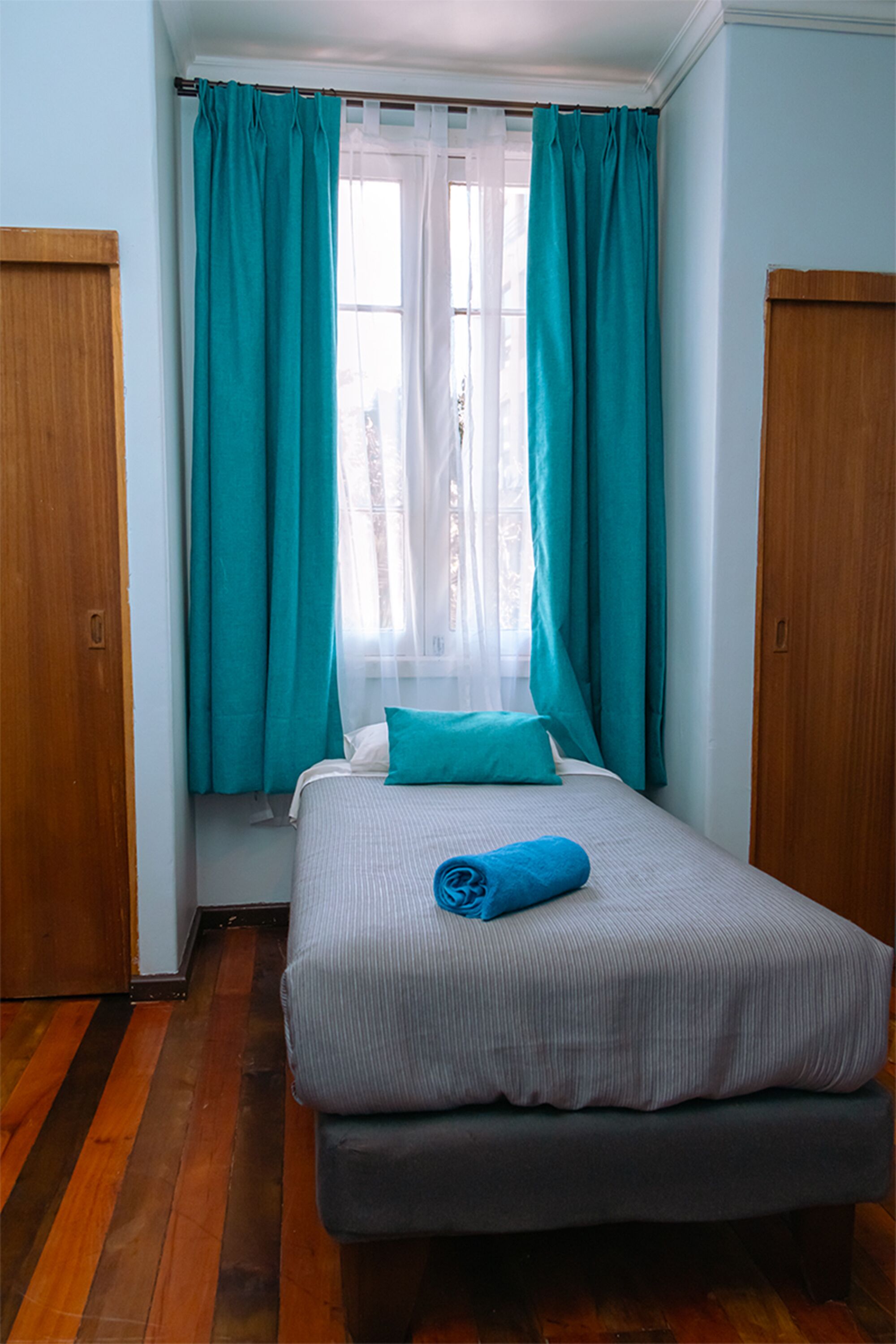 Un dormitorio con cama, cortinas azul verdosas y suelo de madera.
