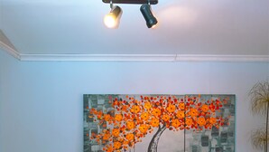 A teal sofa with two pillows, a large painting of a tree with orange flowers, and a potted plant to the left. - Casa del lado Santiago Providencia (Santiago)