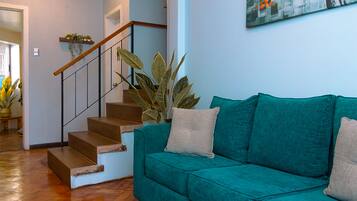 Un sofá color turquesa con cojines, una escalera de madera y una planta en maceta.
