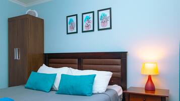 Un dormitorio con cama, mesita de noche con lámpara, armario y tres cuadros en la pared.
