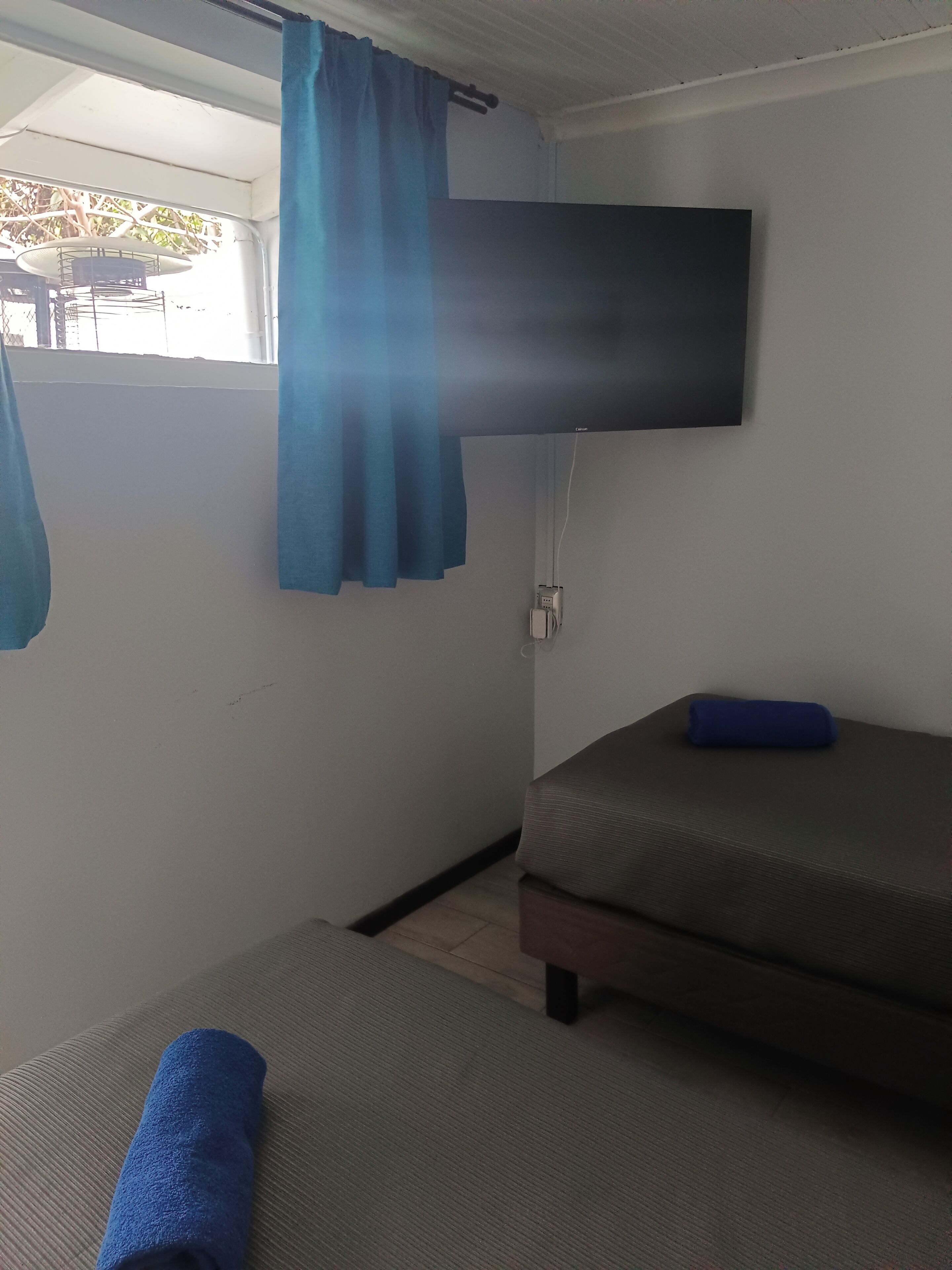 A small room with a bed, a TV mounted on the wall, and a window with curtains.
