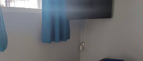 Une petite pièce avec un lit, un téléviseur fixé au mur et une fenêtre avec des rideaux.