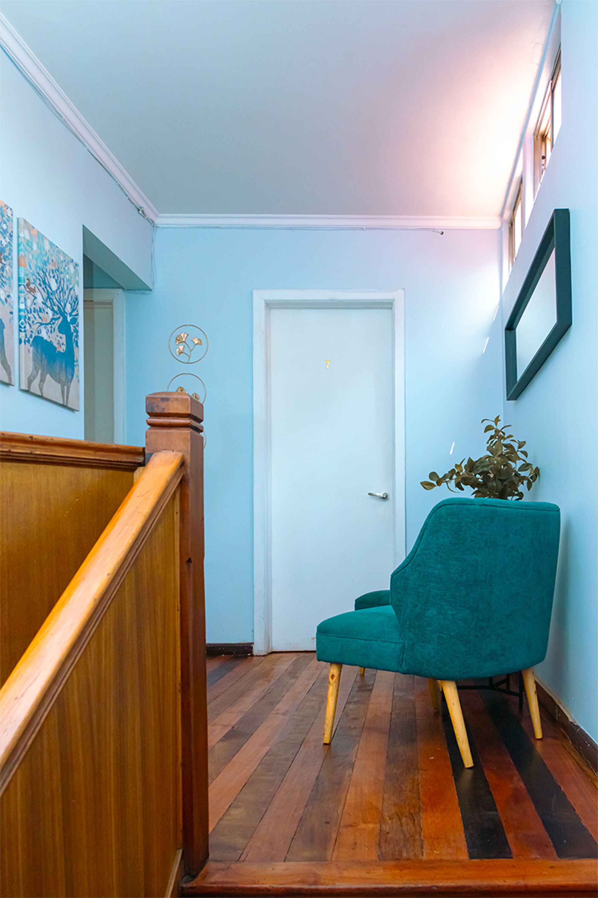 A hallway with a wooden staircase, a teal chair, and a white door.
