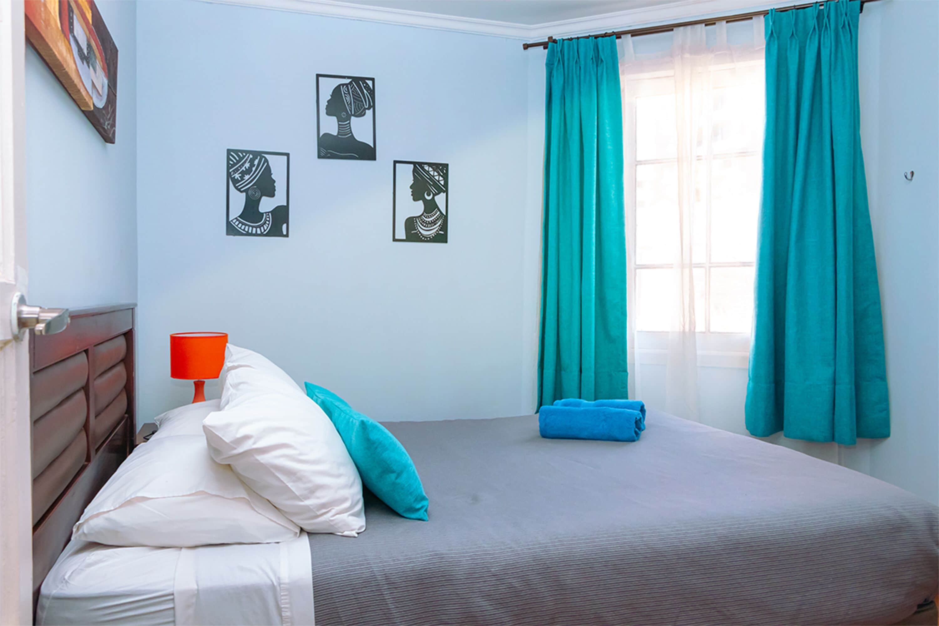 A bedroom with a bed, pillows, a nightstand, a lamp, and artwork on the wall.