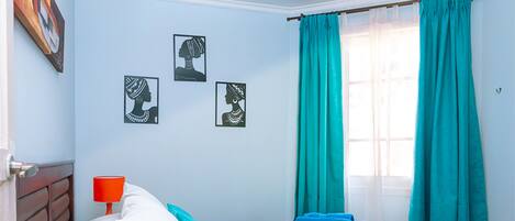 A bedroom with a bed, pillows, a nightstand, a lamp, and artwork on the wall.