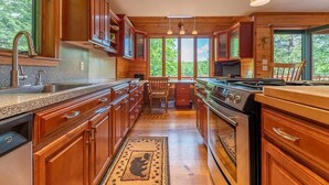 A kitchen with wooden cabinets, a granite countertop, a stove, and a large window offering a view of trees.