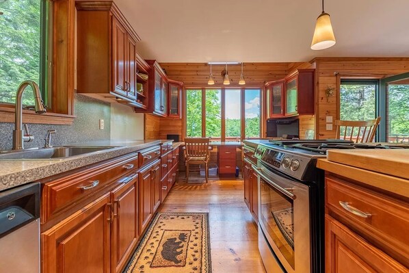 A kitchen with wooden cabinets, a granite countertop, a stove, and a large window offering a view of trees.