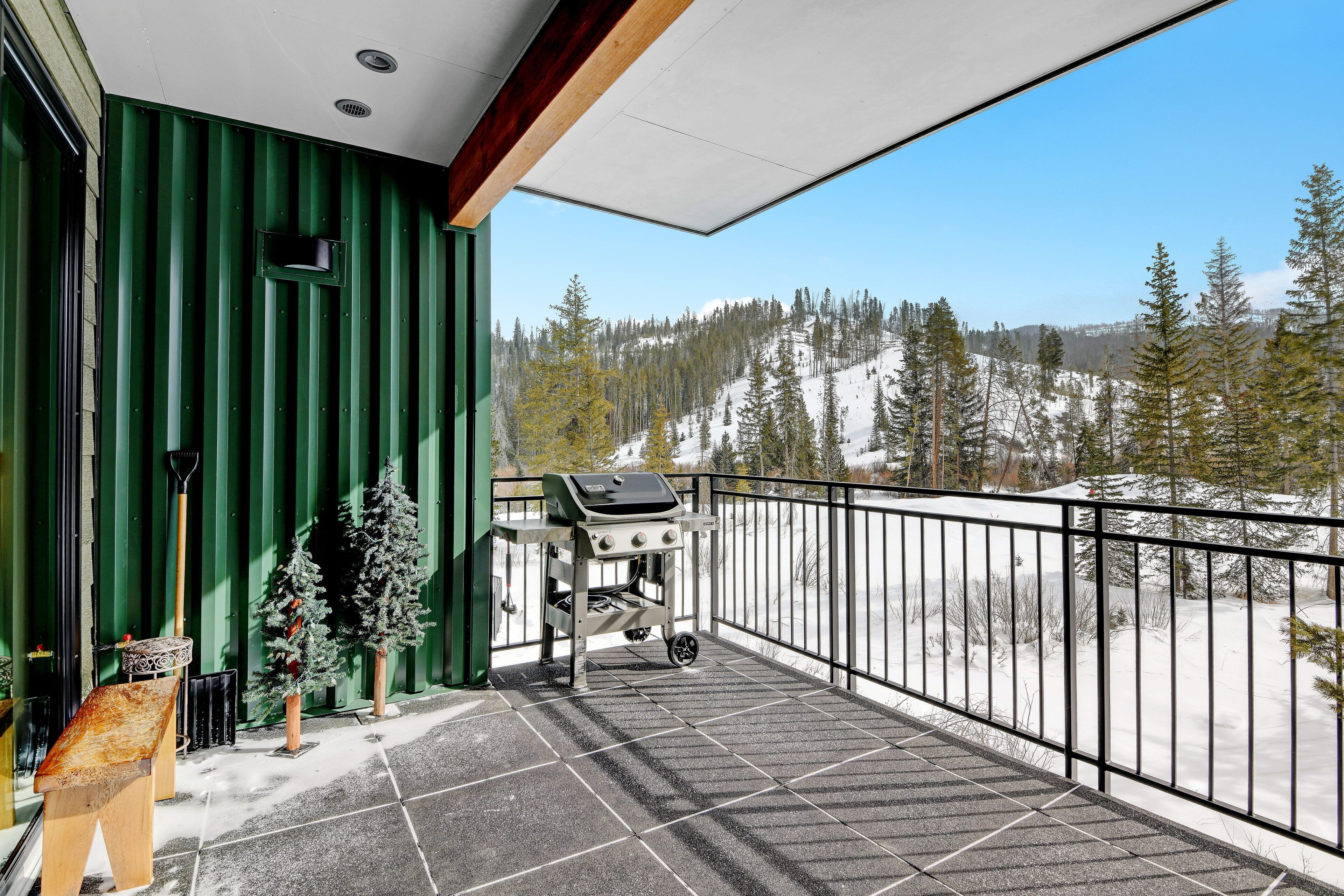 A balcony with a grill, a small Christmas tree, and a bench.