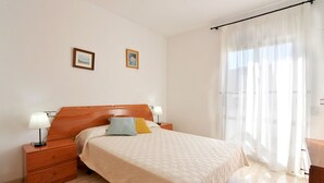 A neatly arranged bedroom with a wooden headboard, a bed with a quilt, two bedside tables with lamps, and a large window with sheer curtains. - CANIGO: House with private pool in l'Escala ideal for families (L'Escala)