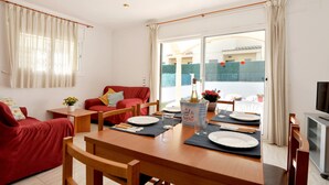 A dining area with a wooden table set for four, a red sofa, and a television on the right. - CANIGO: House with private pool in l'Escala ideal for families (L'Escala)