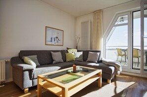 A living room with a sofa, a glass coffee table, and a large window with a view of the sea.