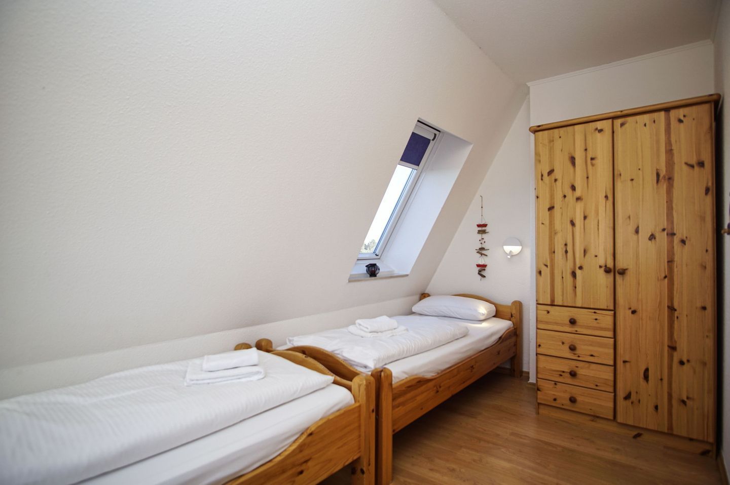 Un petit appartement d’une seule pièce, avec un plafond en pente, un puits de lumière, une armoire en bois et deux lits simples.
