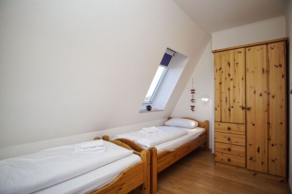 A small, single-room apartment with a sloped ceiling, a skylight, a wooden wardrobe, and two single beds.