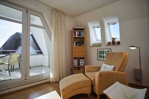 Un salón acogedor con un ventanal grande, una estantería, un sillón cómodo y una lámpara de pie.