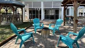 An outdoor patio area with turquoise chairs, a metal fire pit, and a covered seating area. - Right off the main Weeki Wachee River! Beautiful updated home! (Spring Hill)