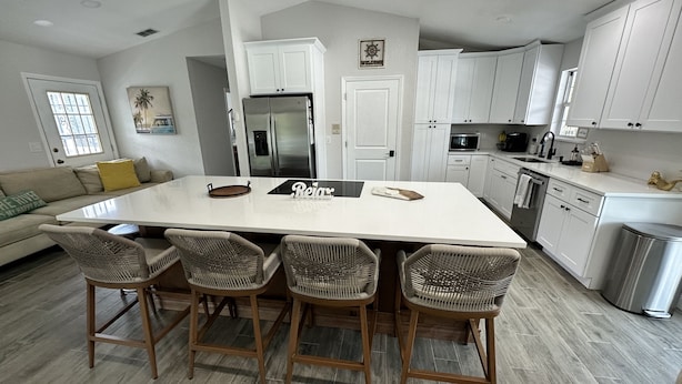 A modern kitchen with white cabinets, a large island with bar stools, stainless steel appliances, and a "Relax" sign on the island. - Right off the main Weeki Wachee River! Beautiful updated home! (Spring Hill)