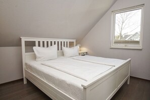 Una cama blanca solitaria en una habitación con techo inclinado y una ventana.