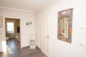 A hallway with a wooden floor, a white door, and a decorative mirror on the wall. - Haus Sternschnuppe—a cozy house with a fireplace, sauna, garden, and patio— (Wiek)