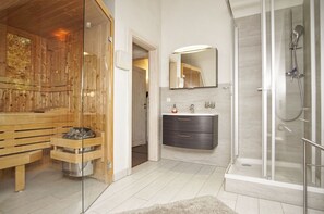 A modern bathroom with a glass shower enclosure, a wooden sauna, and a minimalist vanity.